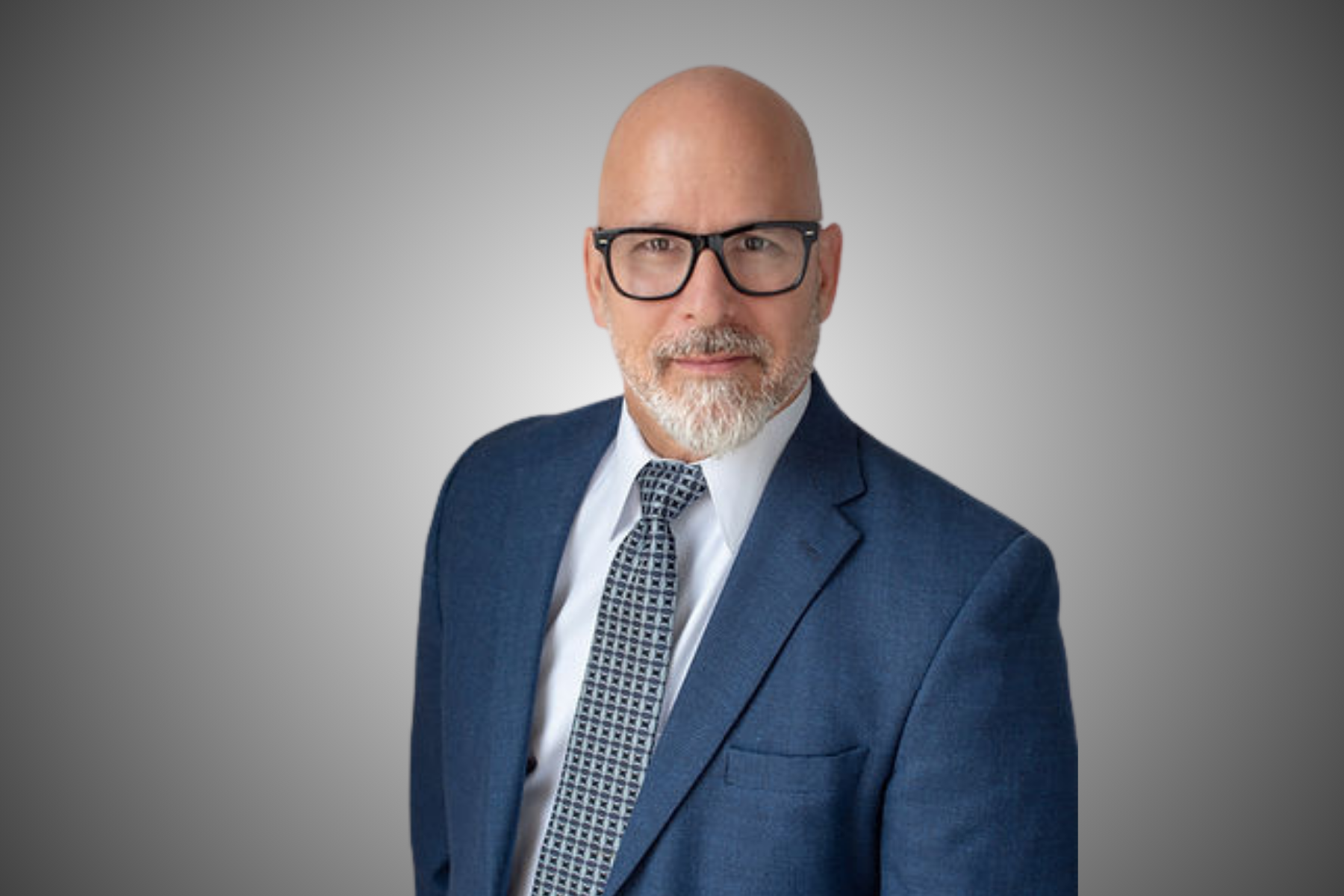 Man in a blue suit and glasses, looking at the camera with a neutral expression.