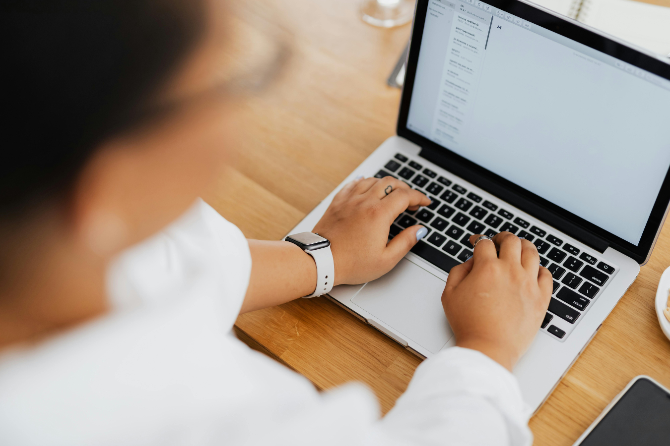 Person typing on a laptop at a wooden desk with a smartphone nearby