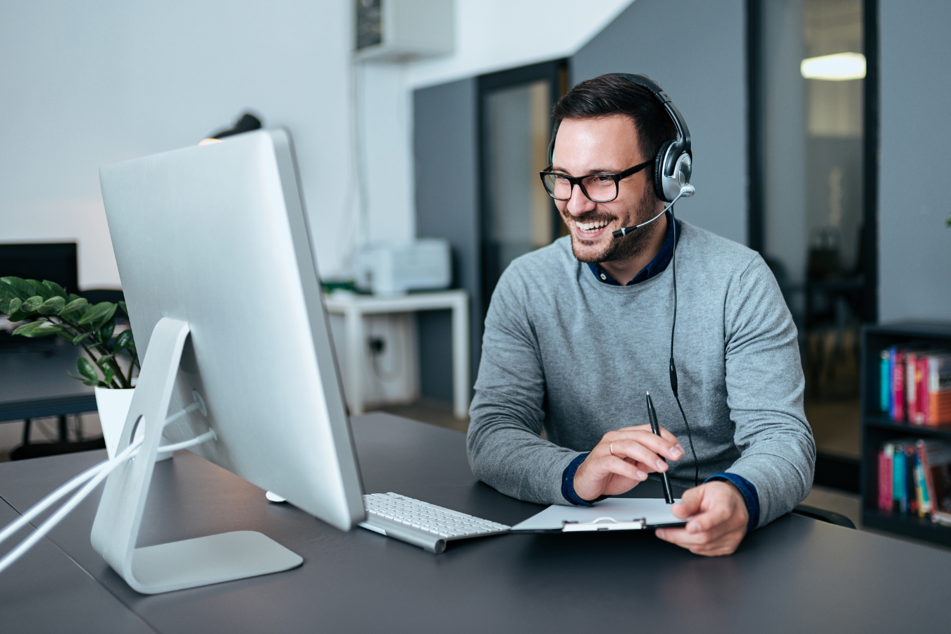 A man wearing headphones is sitting at a desk in front of a computer.