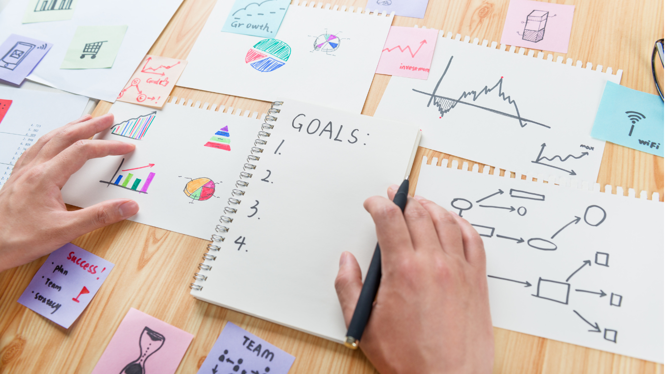 A person is writing goals in a notebook on a wooden table.