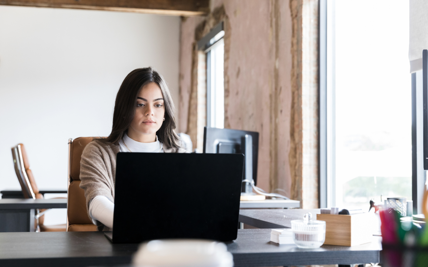 Woman typing on a laptop at a desk in a well-lit office.