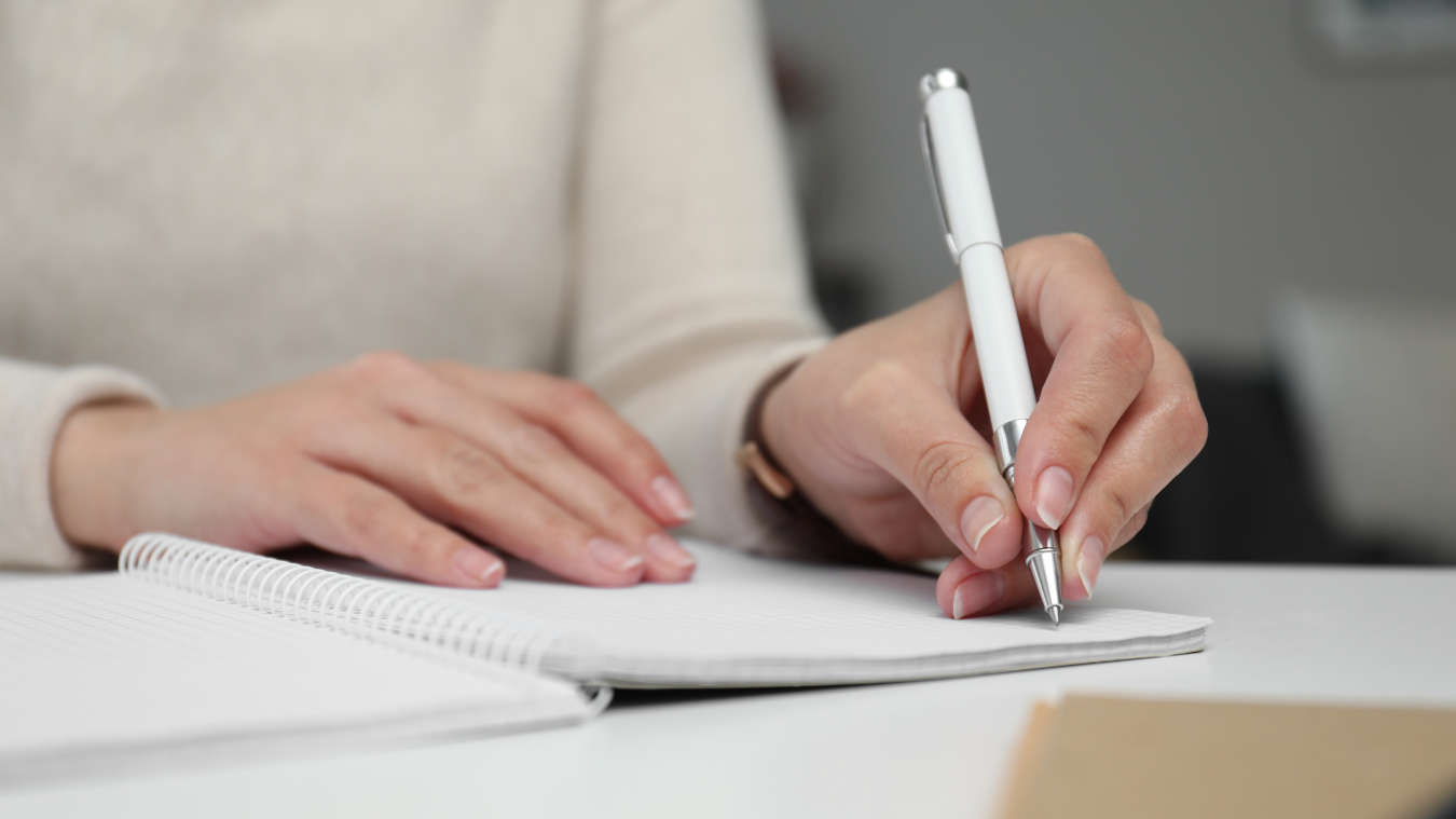 a woman is writing in a notebook with a pen