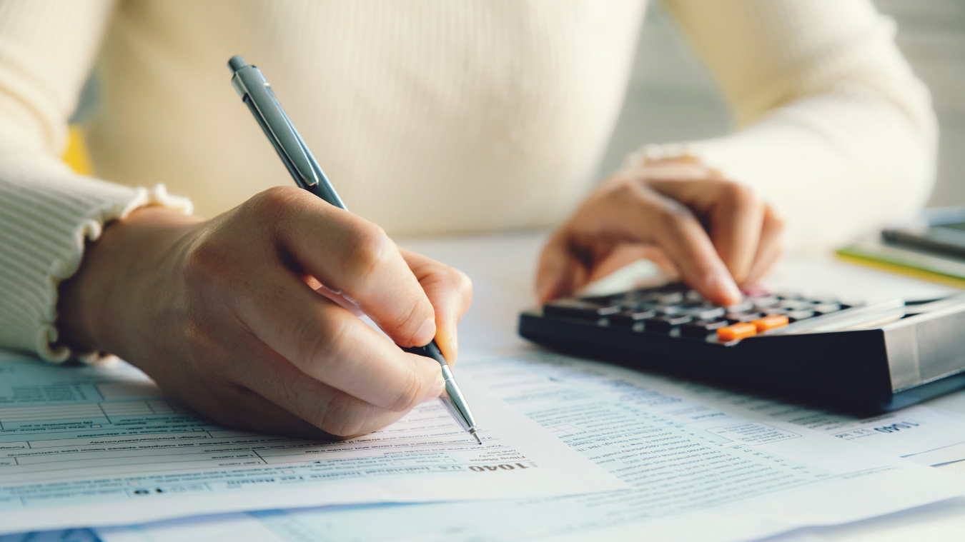 A person is writing on a piece of paper while using a calculator.
