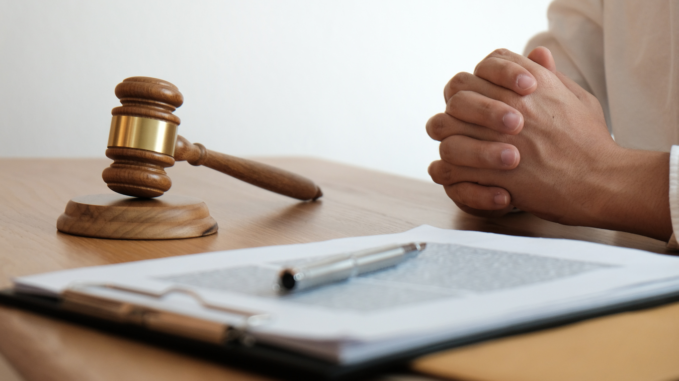 A person is sitting at a table with their hands folded in front of a judge 's gavel.