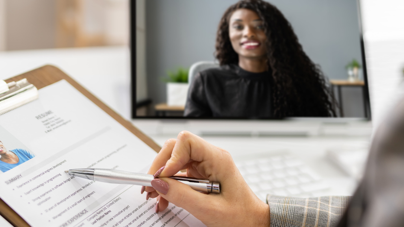 A woman is sitting in front of a laptop while holding a pen and a clipboard.