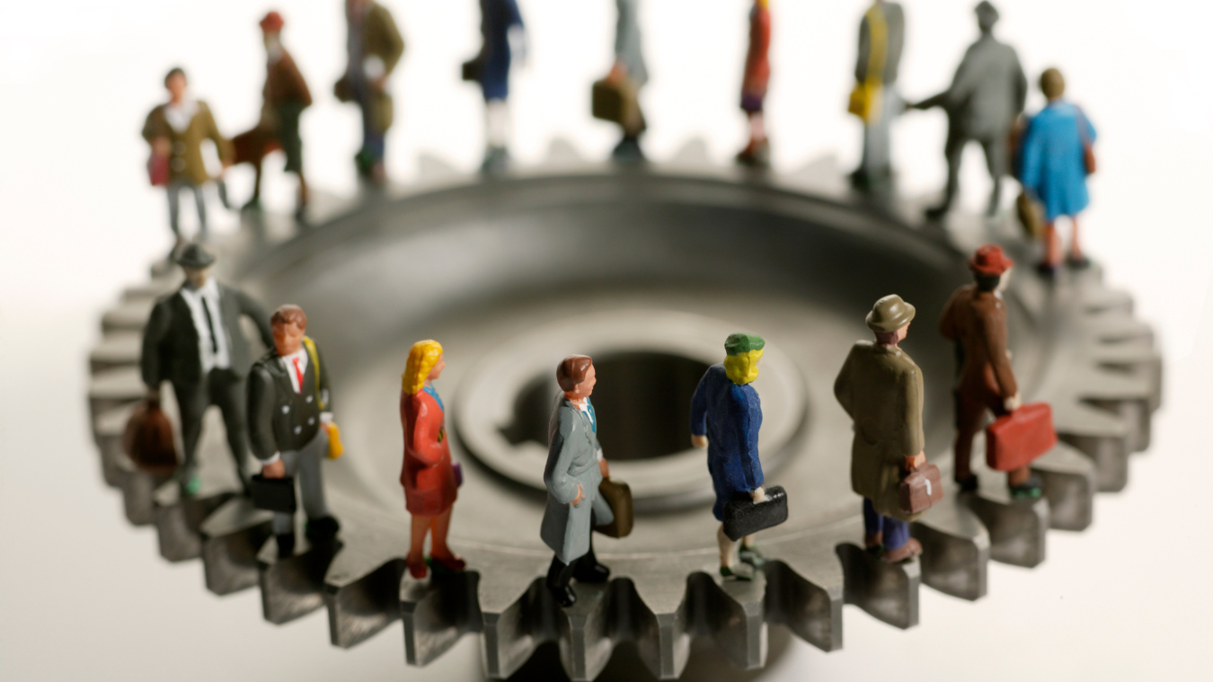 A group of miniature people are standing around a gear.