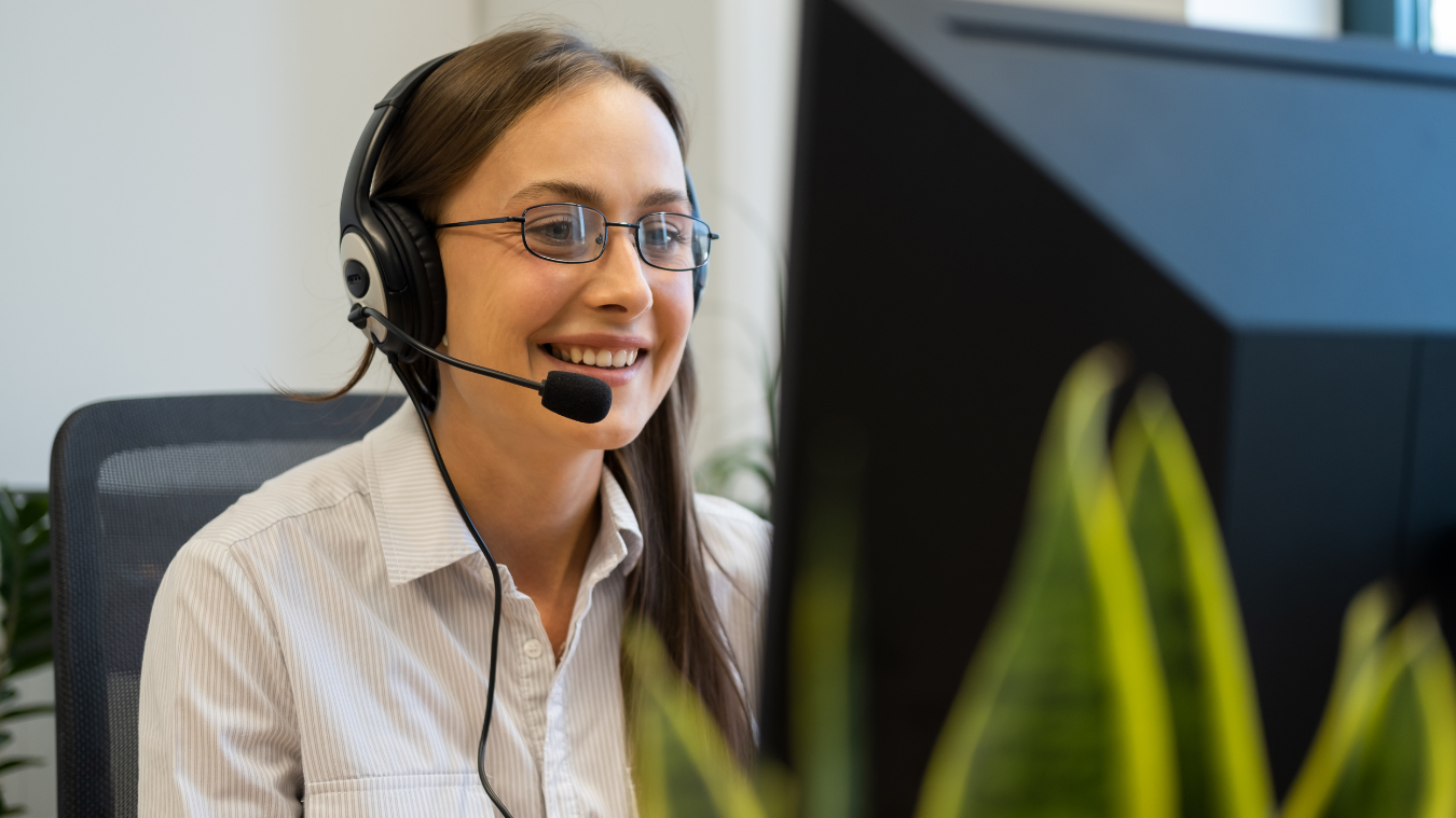 A woman wearing headphones and glasses is sitting in front of a computer.