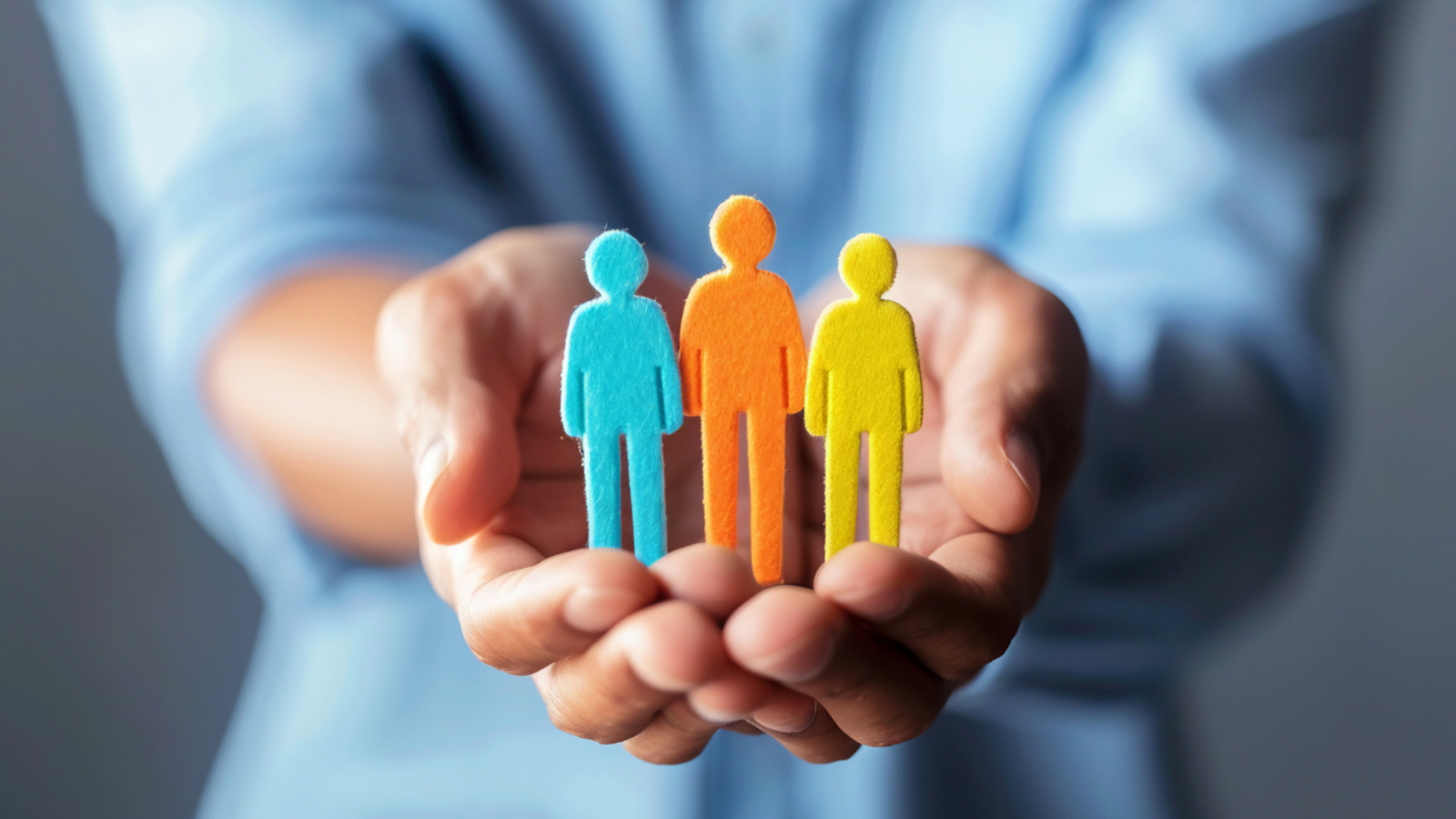 Hands cupped, holding three colorful human figure cutouts: blue, orange, and yellow, representing people.