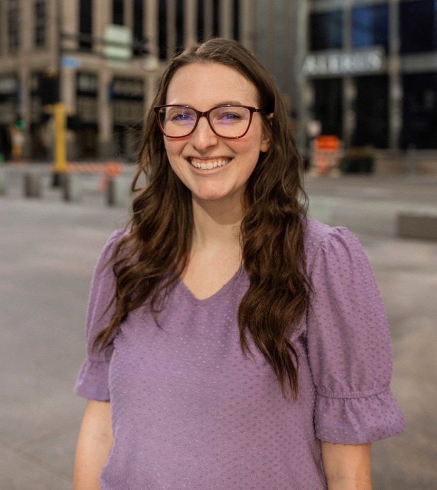 A woman wearing glasses and a purple shirt is smiling for the camera.
