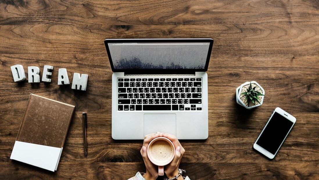 A person is holding a cup of coffee in front of a laptop computer.