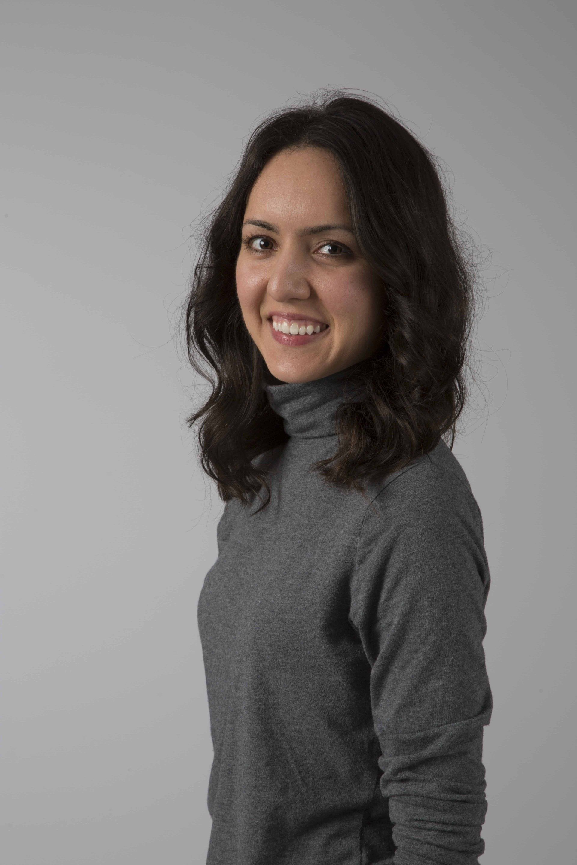 A woman is wearing a gray turtleneck sweater and smiling.