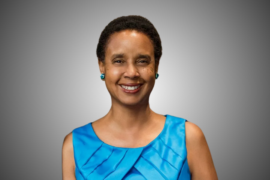 Woman smiling, wearing a blue sleeveless top, small blue earrings, against a gray gradient background.
