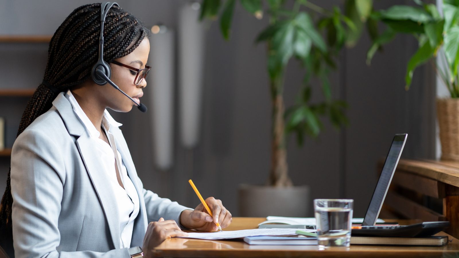 A woman wearing a headset is sitting at a desk in front of a laptop computer.