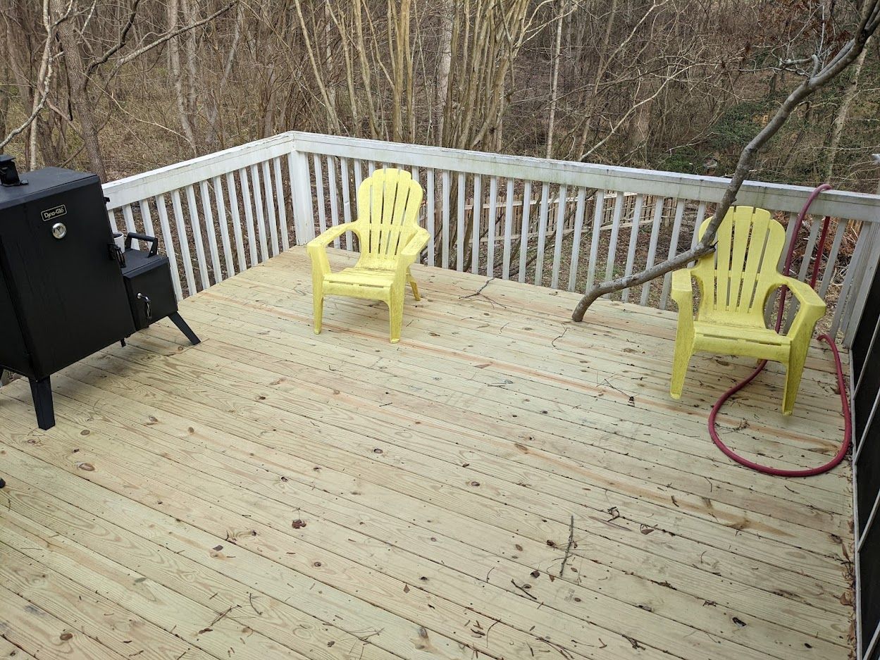 A wooden deck with two yellow chairs and a grill.