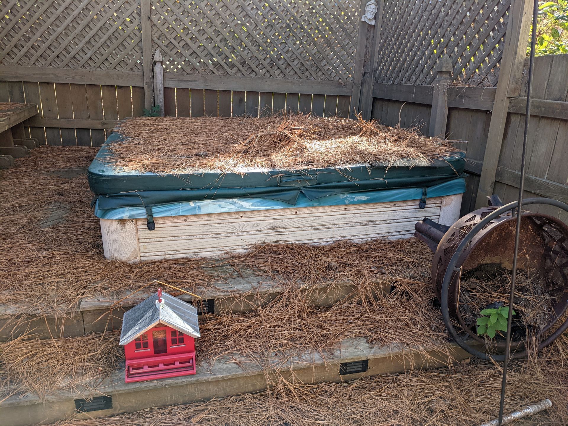 A hot tub is covered in hay and a birdhouse is sitting next to it.