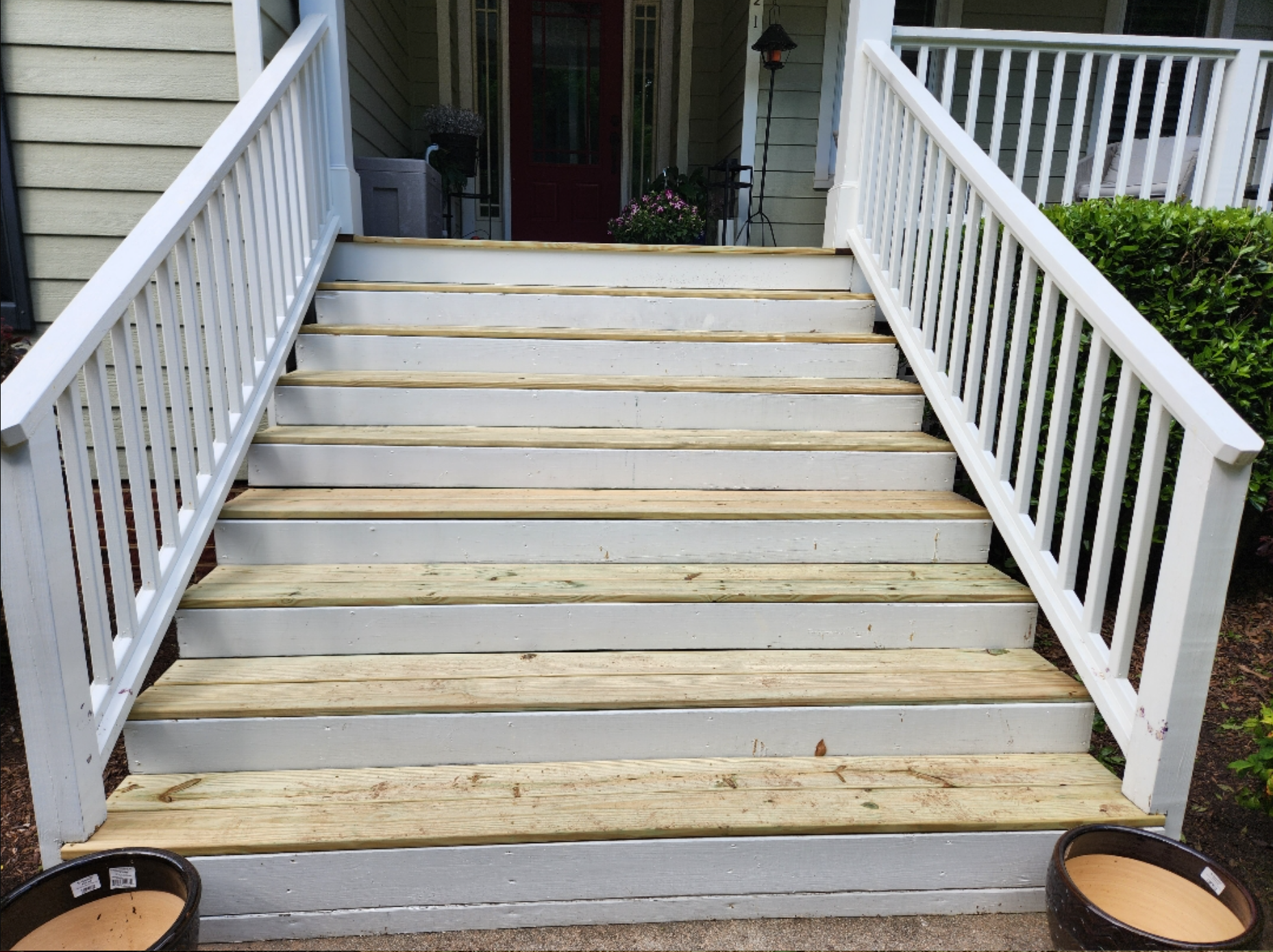 A set of wooden stairs leading up to a porch with a white railing.