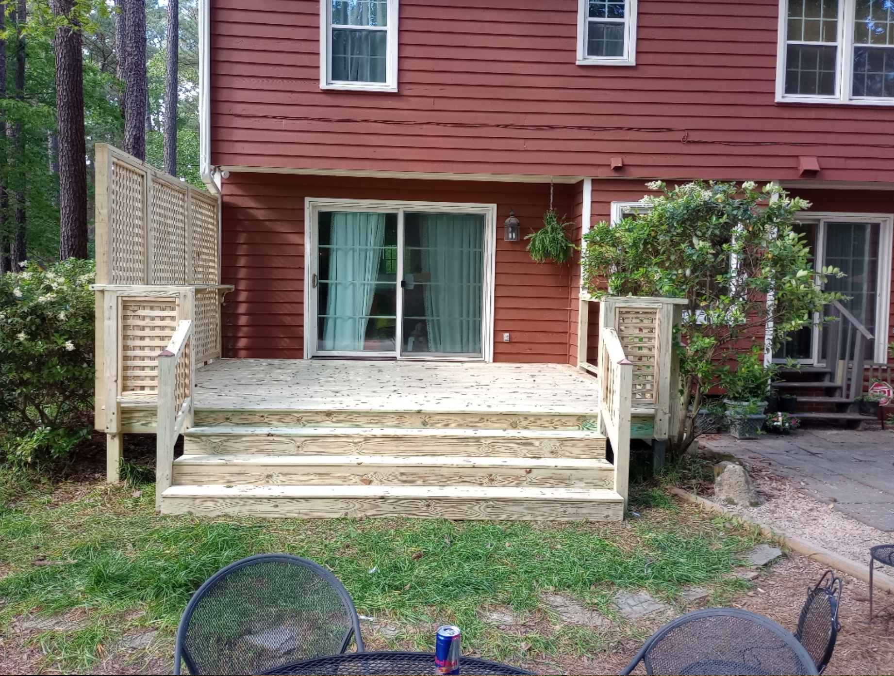 A wooden deck with stairs and a table and chairs in front of a red house.