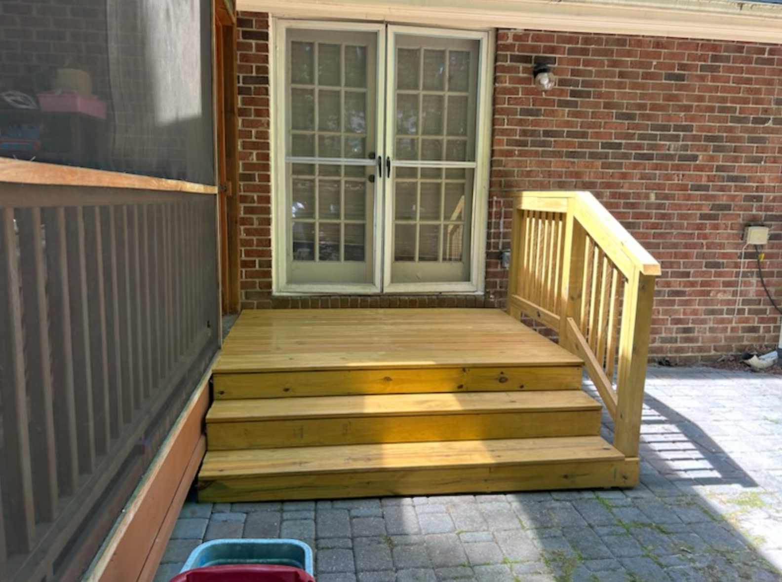 A wooden deck with stairs leading up to a screened in porch.