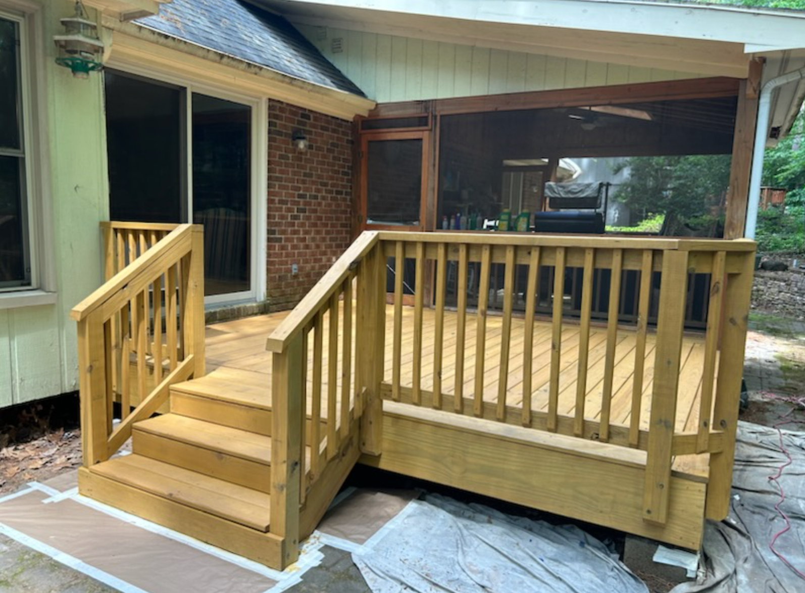 A wooden deck with stairs and a screened in porch next to a house.