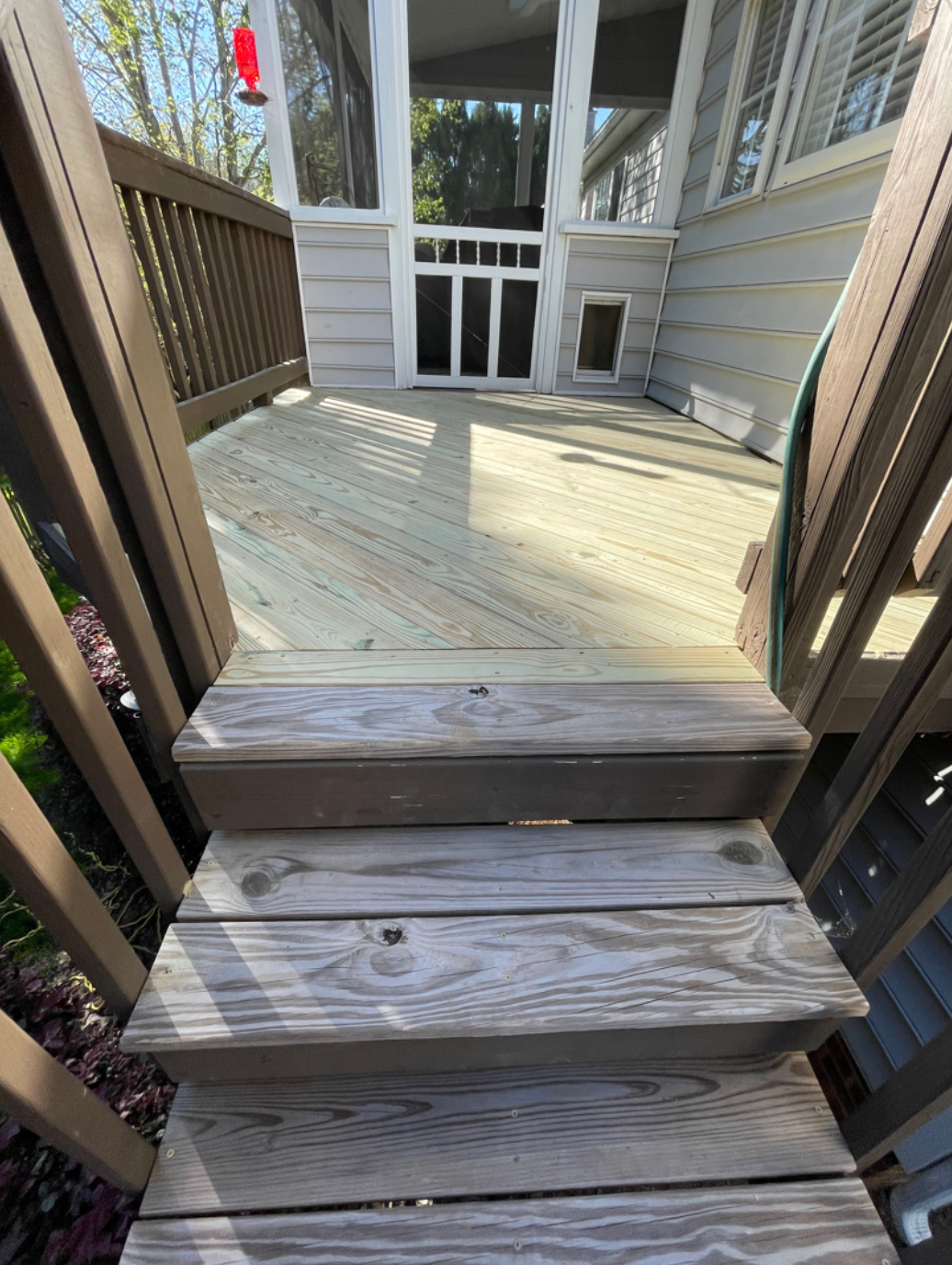 A wooden deck with stairs leading up to it and a screened in porch.