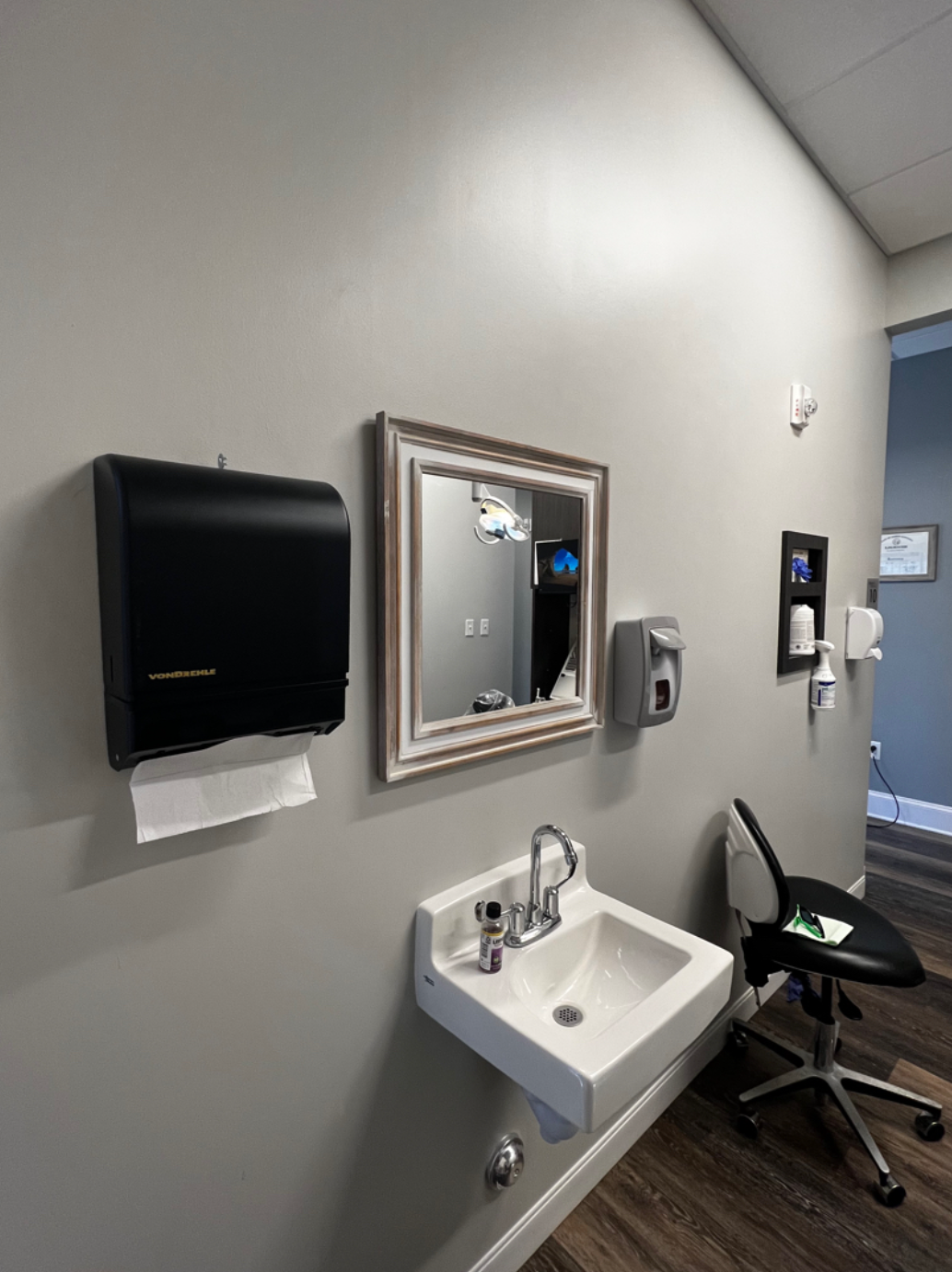 A bathroom with a sink , mirror , and paper towels.