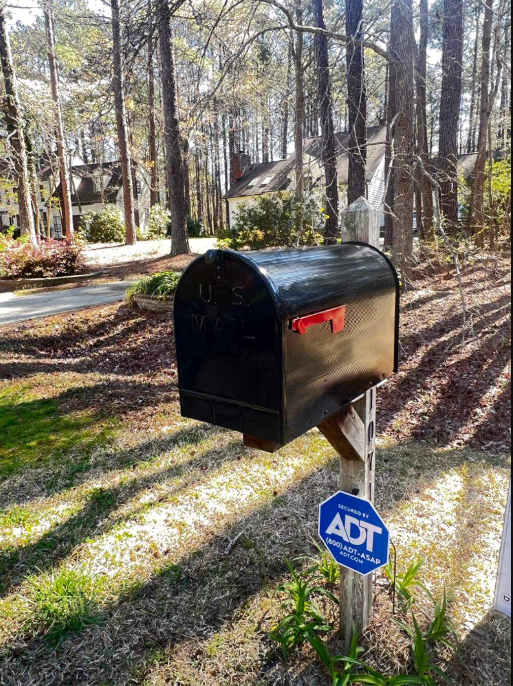 A black mailbox is sitting next to a sign that says adt.