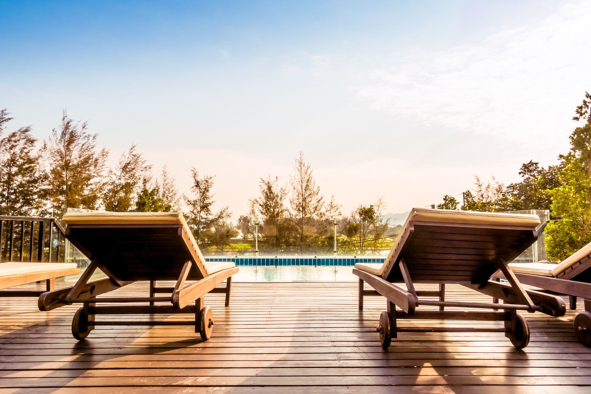 Three lounge chairs are sitting on a wooden deck next to a swimming pool.
