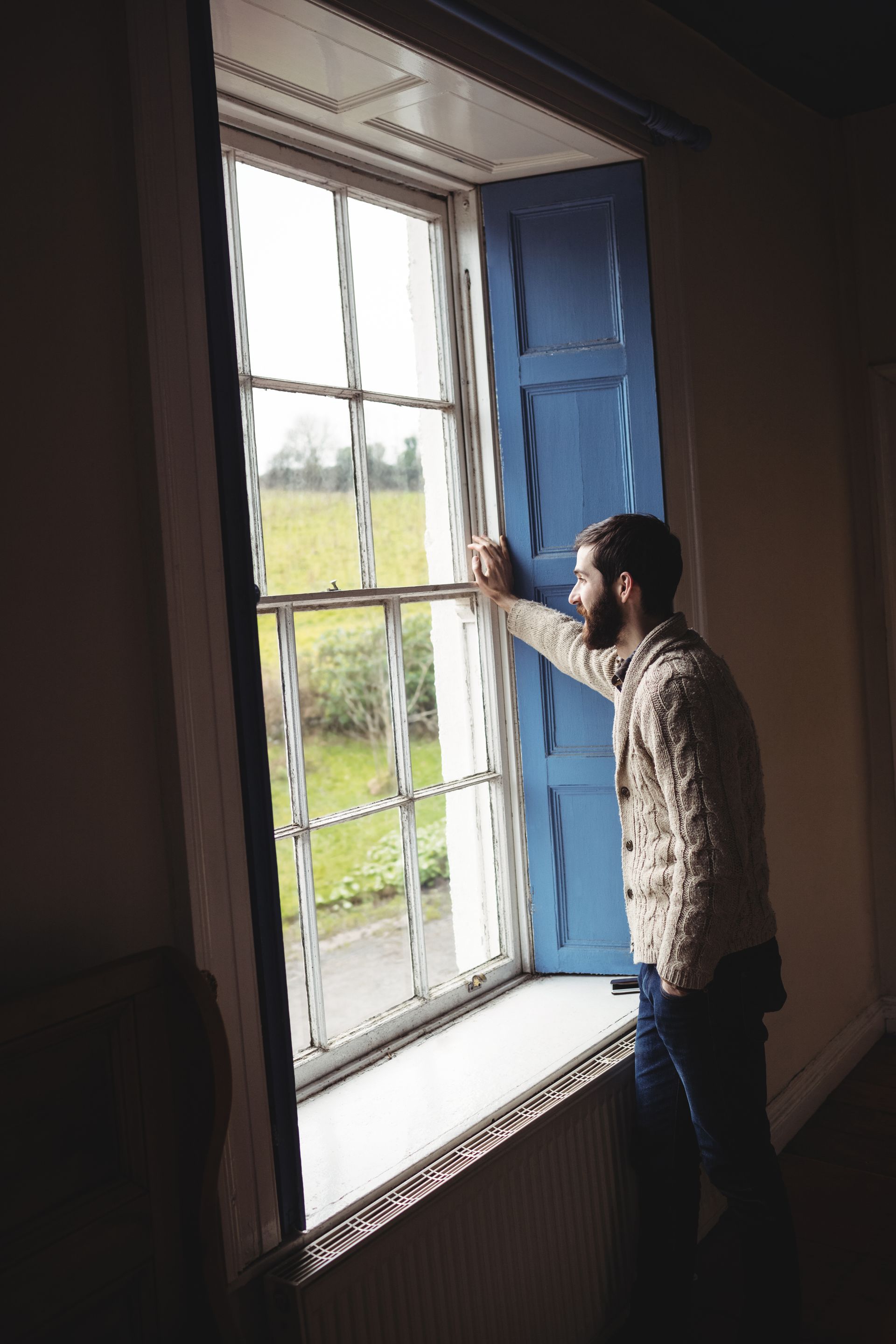 A man is looking out of a window with blue shutters.