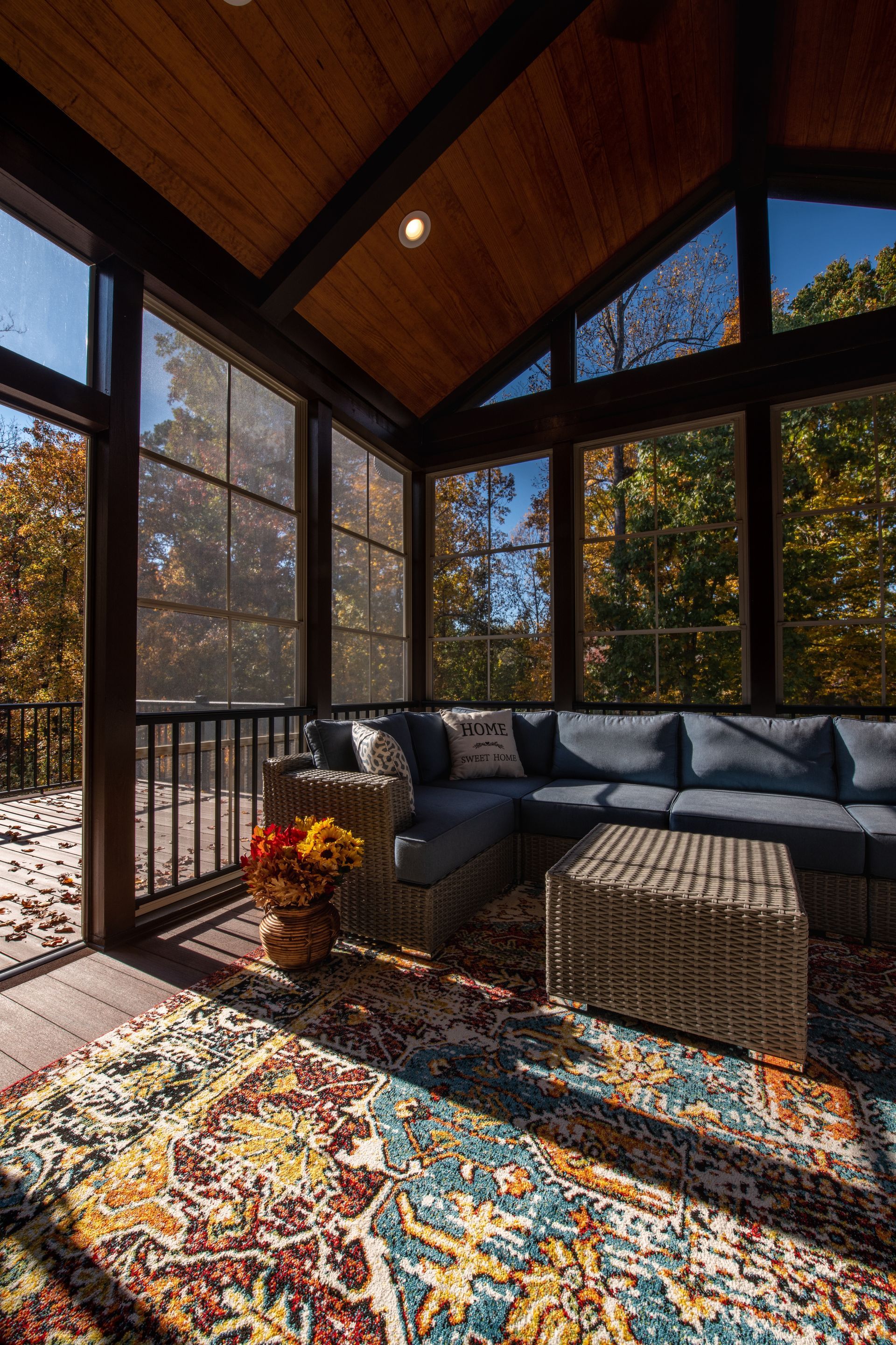 A screened in porch with a couch , chair , table and rug.