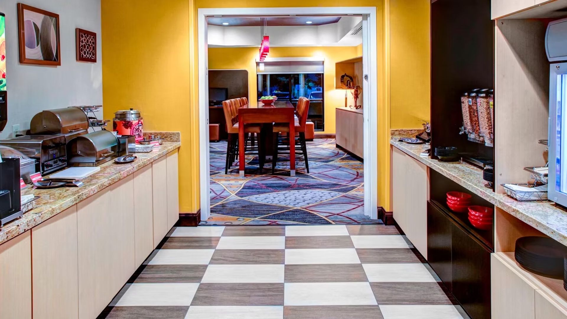 Hotel breakfast area with yellow walls, tile floor, and hallway to dining area.