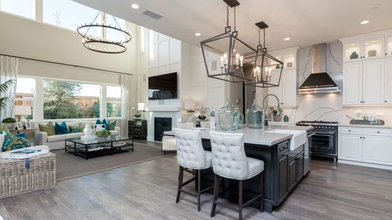 Open-concept kitchen and living room. White cabinets, black island with two chairs. Bright, airy space with large windows.