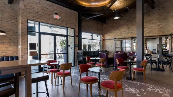 Interior view of a cafe with brick walls, tables and chairs, and large windows.