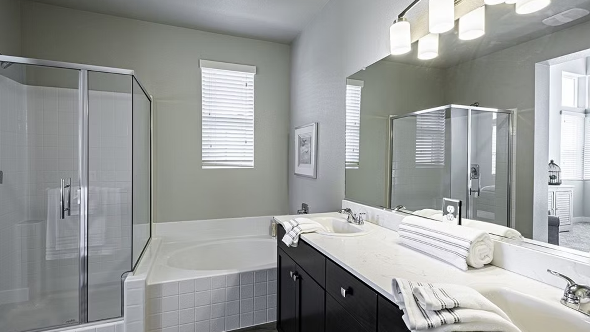 Bathroom with glass shower, double vanity, bathtub, and large mirror. Neutral tones, modern design.