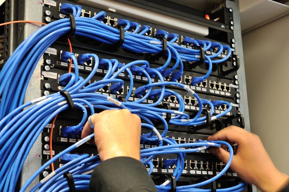 Hands Connecting Blue Network Cables To Server Rack — Superior Wifi in East Ballina, NSW