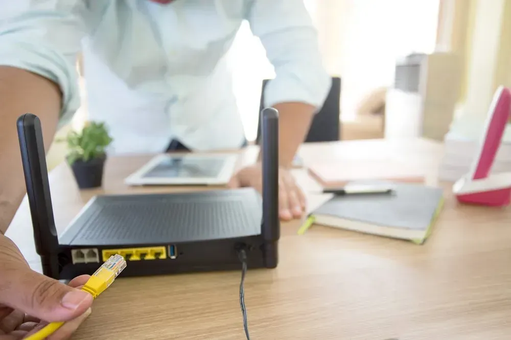 Person Connecting Yellow Ethernet Cable To Black Router — Superior Wifi in East Ballina, NSW