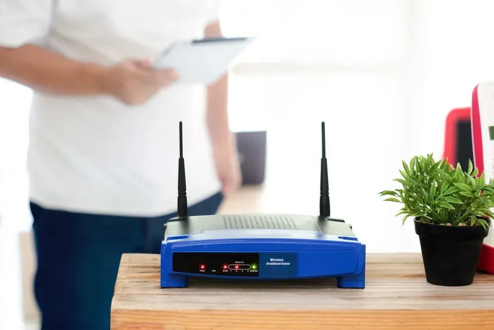 Blue Wifi Router On Wooden Desk With Person Holding Tablet — Superior Wifi in East Ballina, NSW