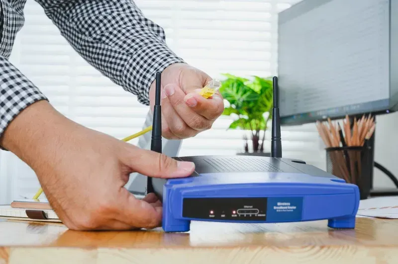 Person Connecting a Yellow Ethernet Cable to a Blue Router With Two Antennas — Superior Wifi in Lennox Head, NSW