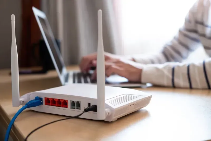 White Wi-fi Router With Blue and Black Cables Connected, Person Using Laptop — Superior Wifi in Lennox Head, NSW