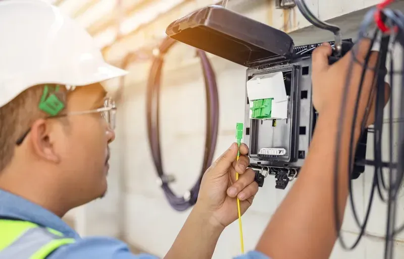 A Technician in a Hard Hat Connecting Fiber Optic Cable in an Outdoor Utility Box — Superior Wifi in Ballina, NSW