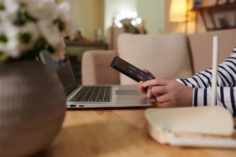 Person Using a Laptop and Phone, Router on Table. Neutral Setting With Flowers and Couch — Superior Wifi in Lennox Head, NSW