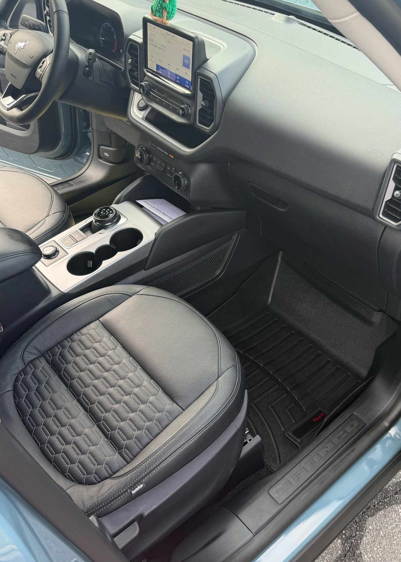 Car interior with open door, black quilted seat cover, touchscreen display, and blue exterior paint