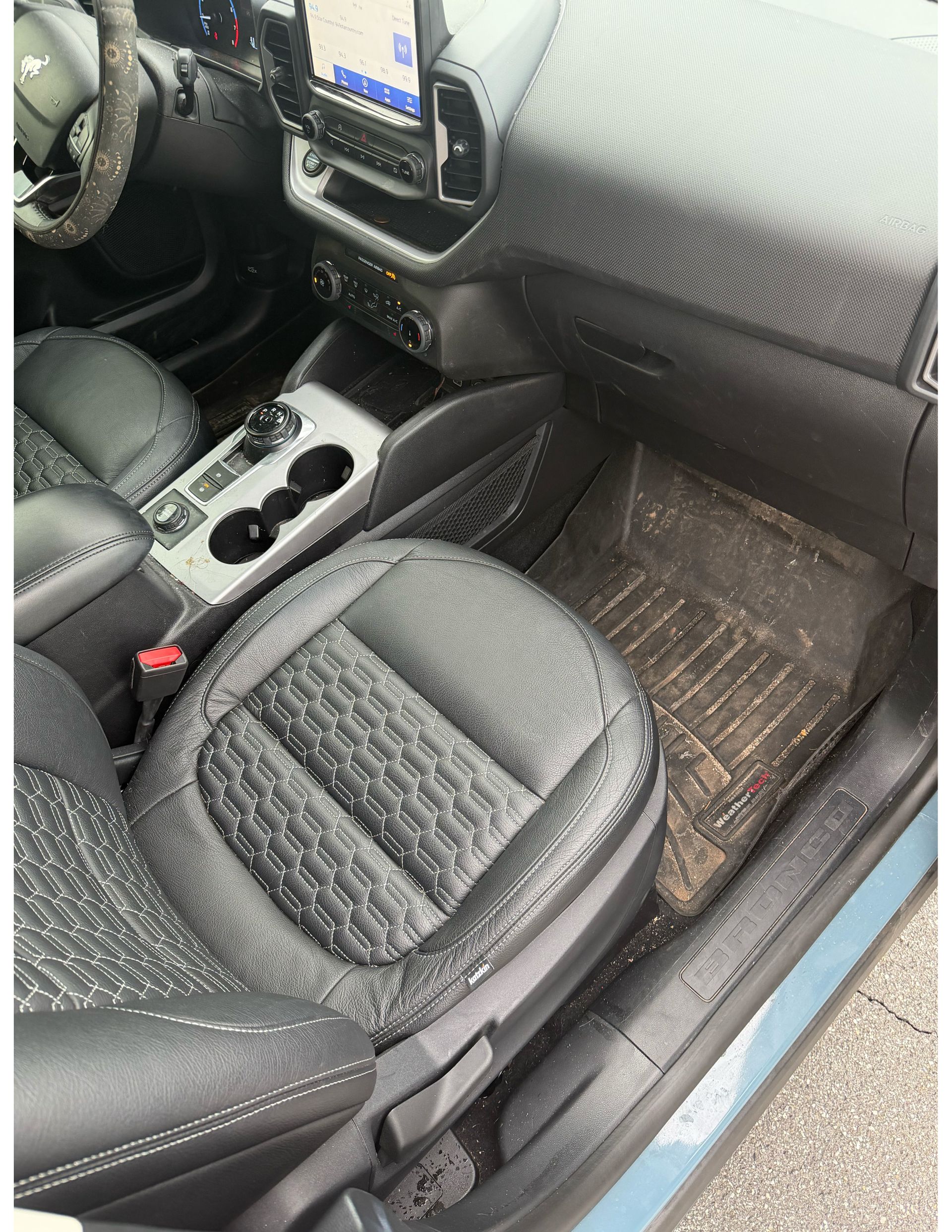 Car interior with black leather seats, center console cup holders, and dashboard visible on the passenger side.