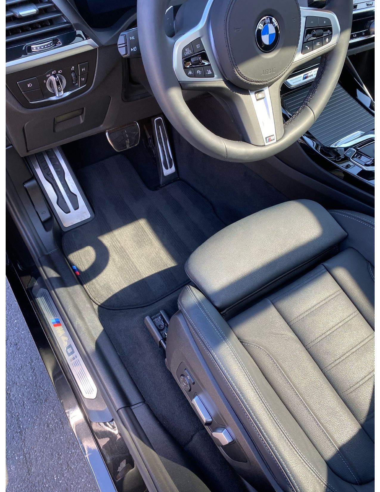 BMW car interior with black leather seats, steering wheel, and sunlit driver’s footwell