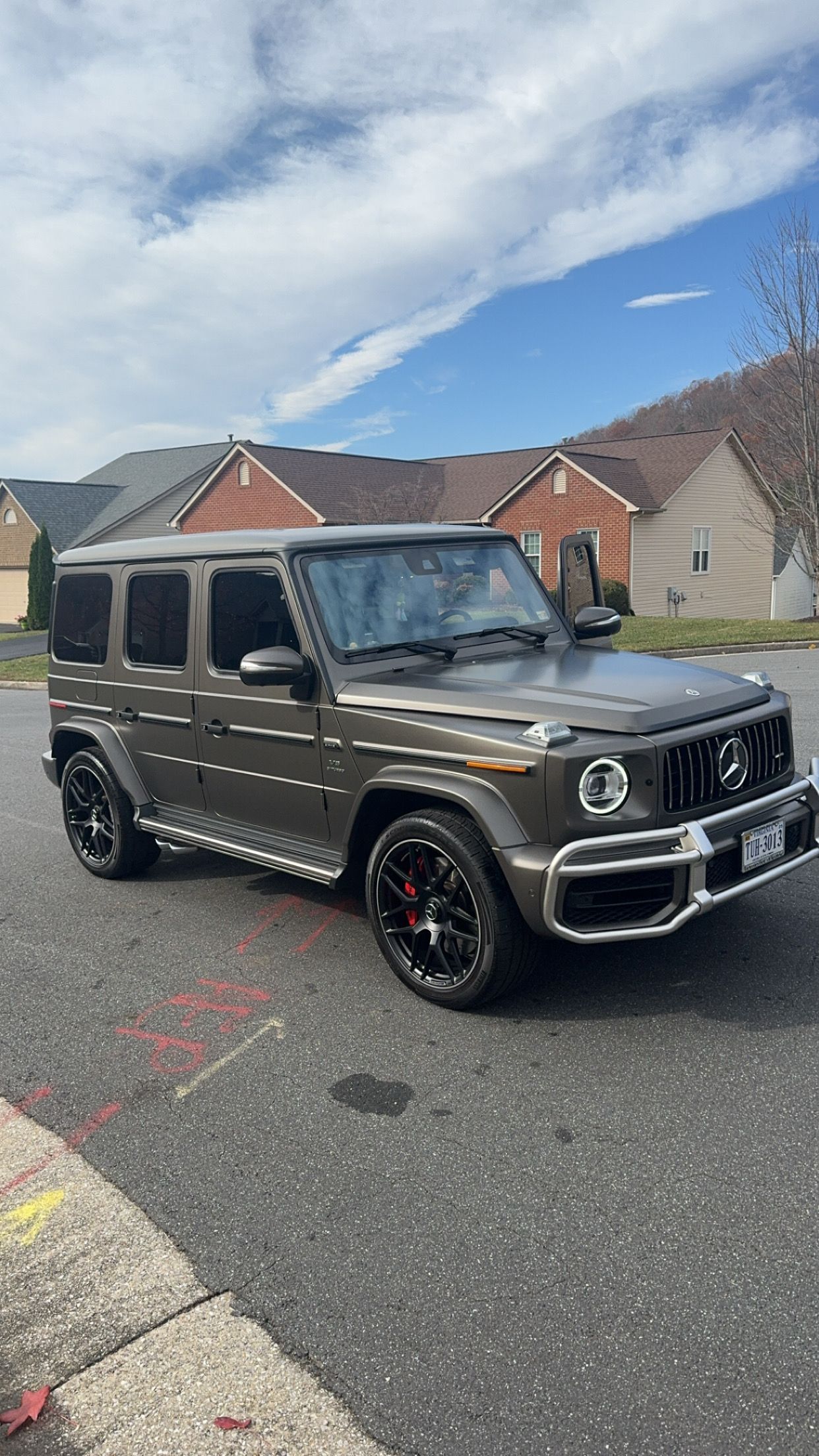 Black Mercedes G-Class SUV parked on a suburban street under a partly cloudy sky