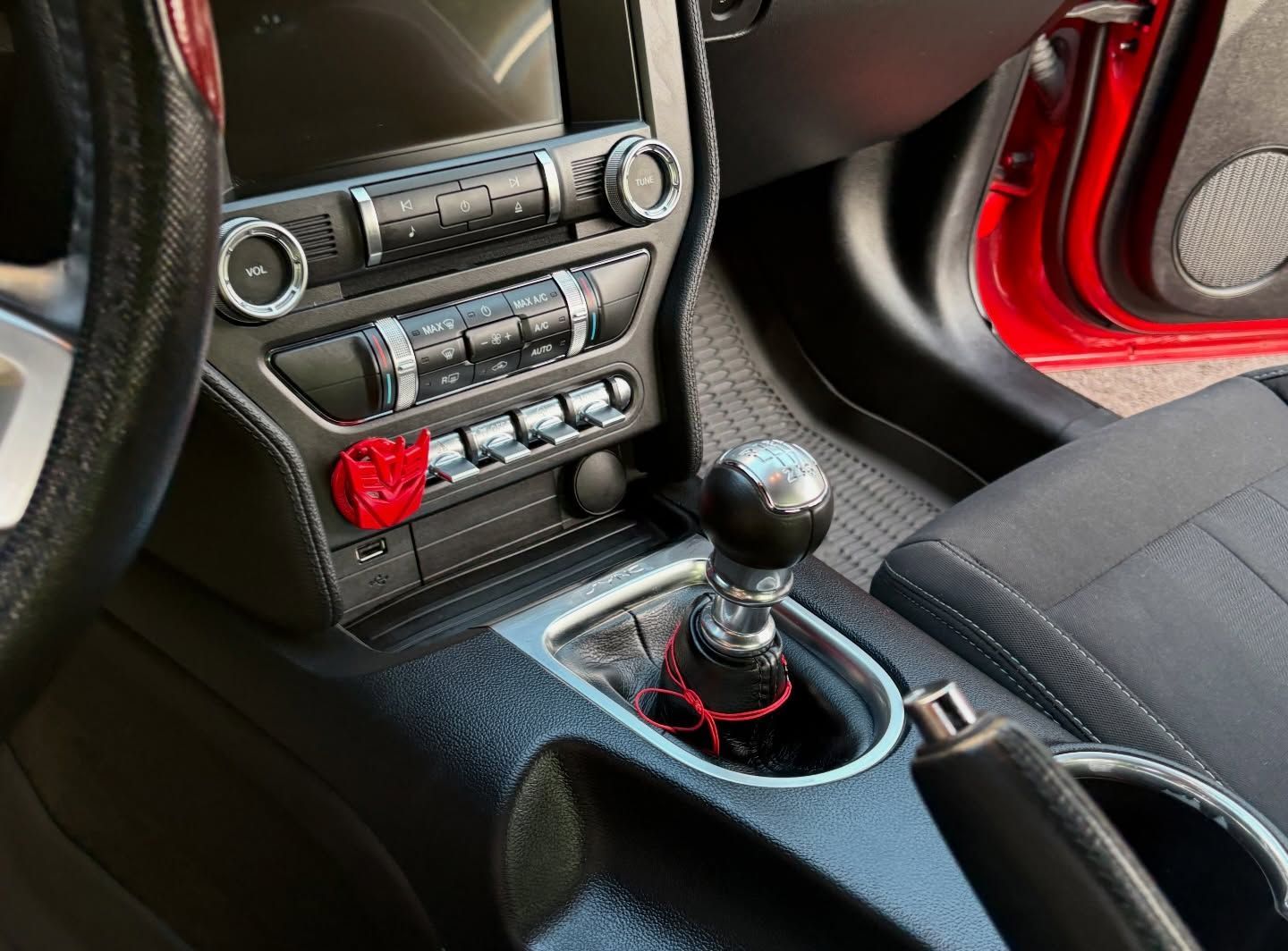 Hand vacuum cleaning a car’s black floor mat near the pedals