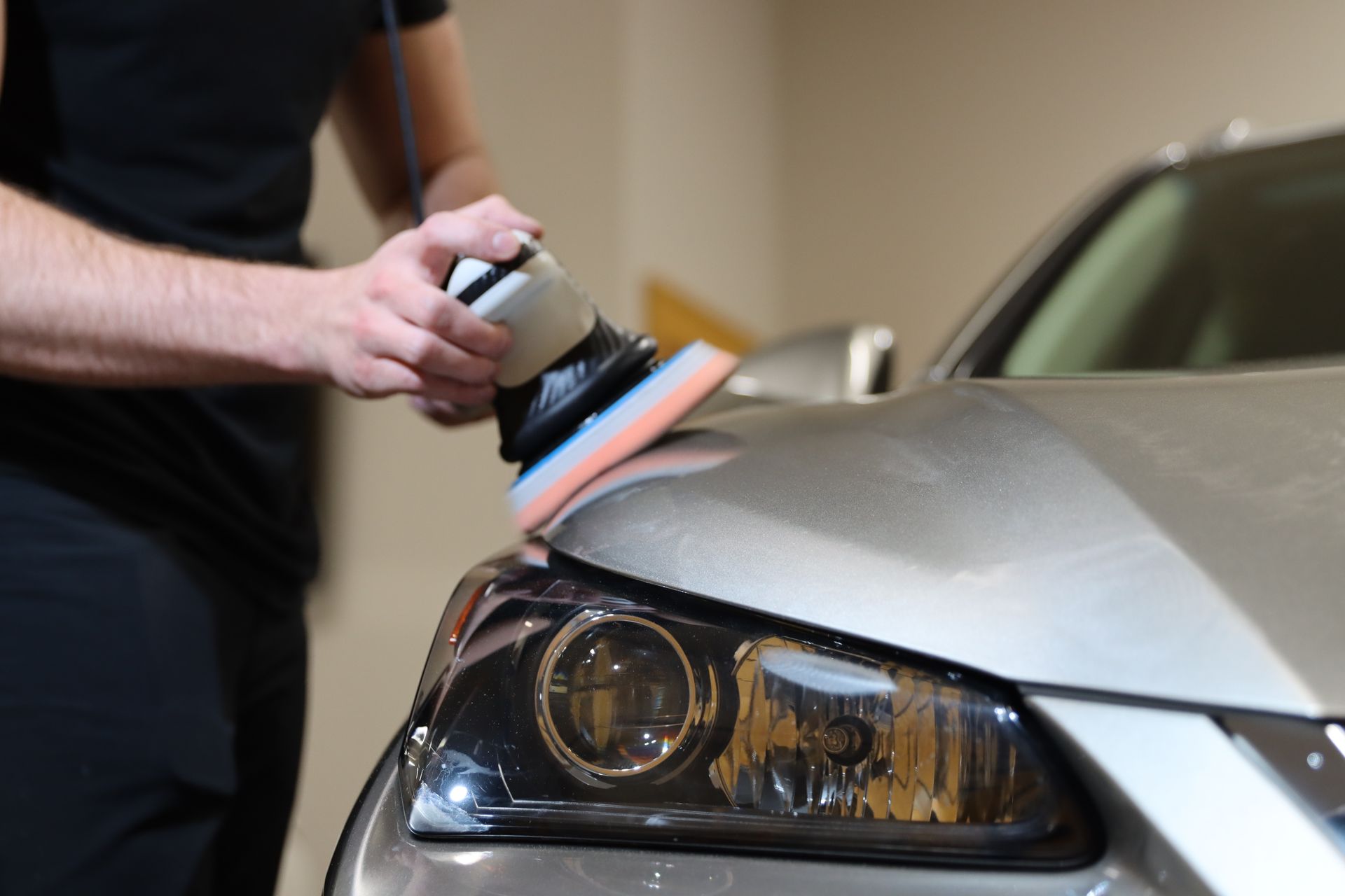 Person polishing a silver car hood with a power buffer in a garage