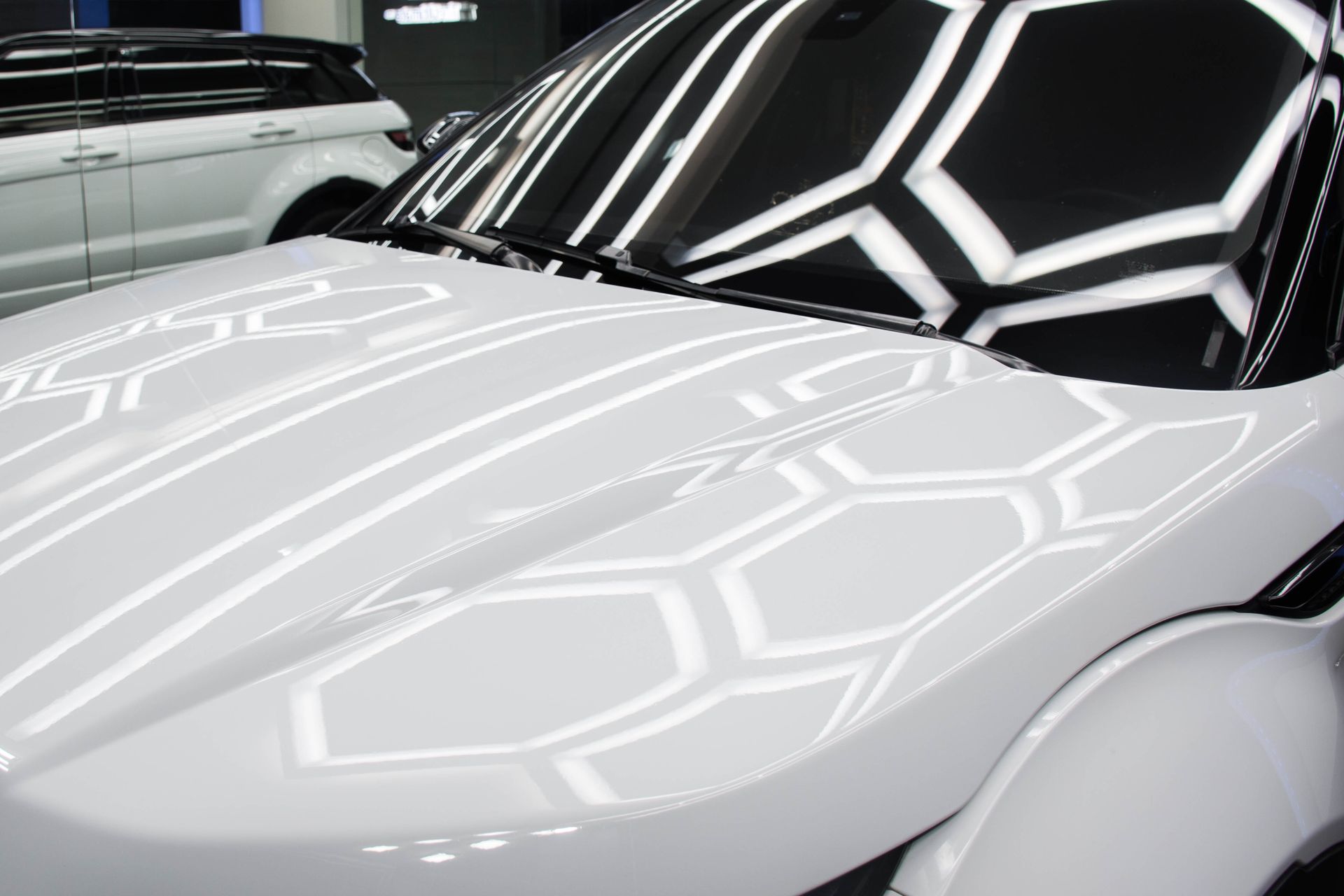 Close-up of a white sports car with a black windshield reflecting bright geometric lights