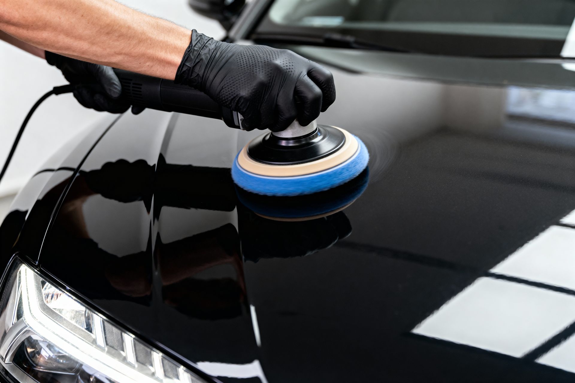 Person polishing a black car hood with a buffer, creating a glossy finish