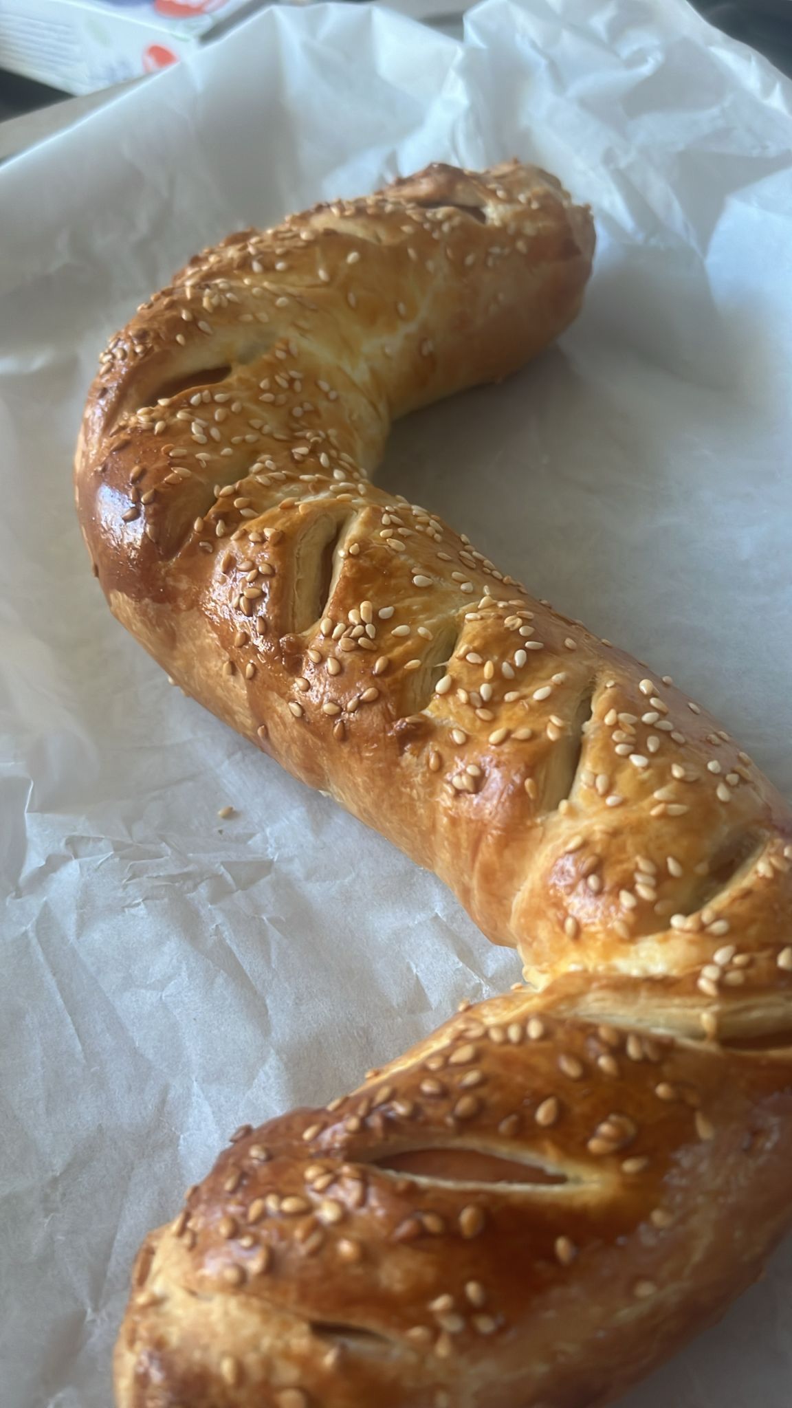 Een goudbruin, gedraaid gebakje bestrooid met sesamzaadjes, rustend op wit bakpapier.