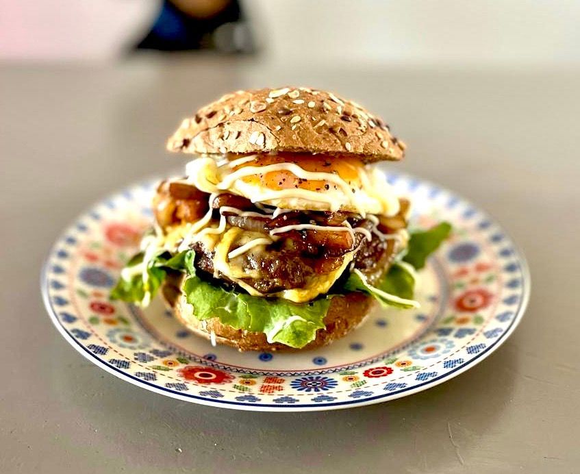 Een gastronomische burger met een gebakken ei, sla en saus op een meergranenbroodje, geserveerd op een kleurrijk, decoratief bord.